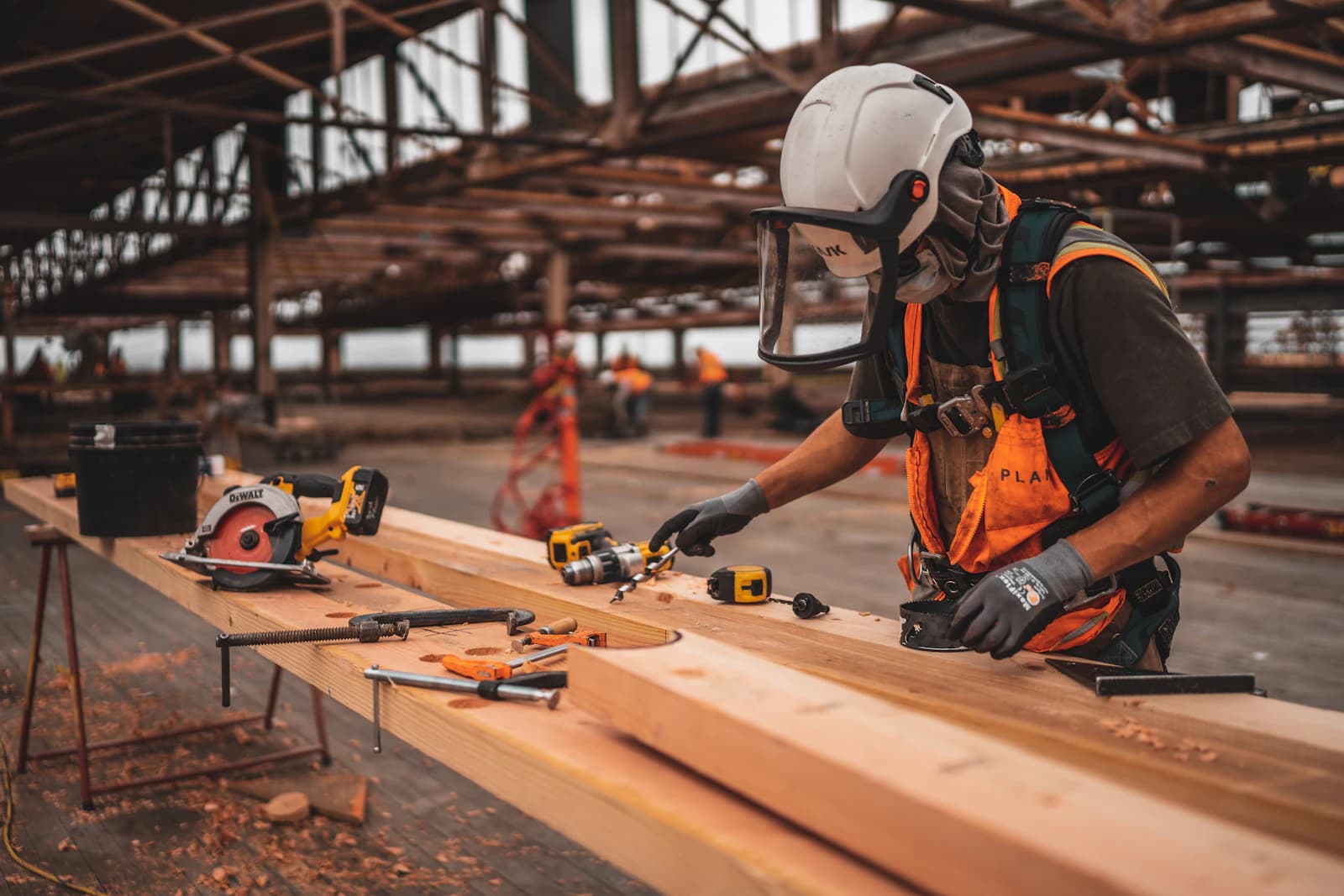 Artisan casqué en gilet orange travaillant le bois sur un chantier